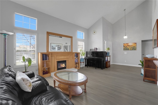 living room with high vaulted ceiling, baseboards, wood finished floors, and a warm lit fireplace