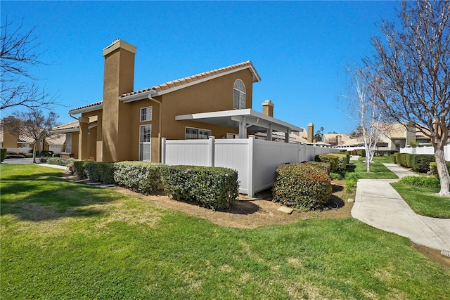 back of property with stucco siding, a chimney, a tiled roof, fence, and a lawn