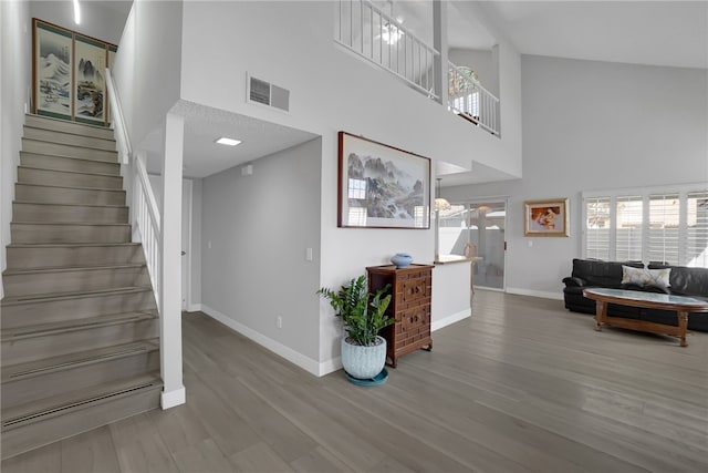 foyer with a towering ceiling, baseboards, stairway, visible vents, and wood finished floors