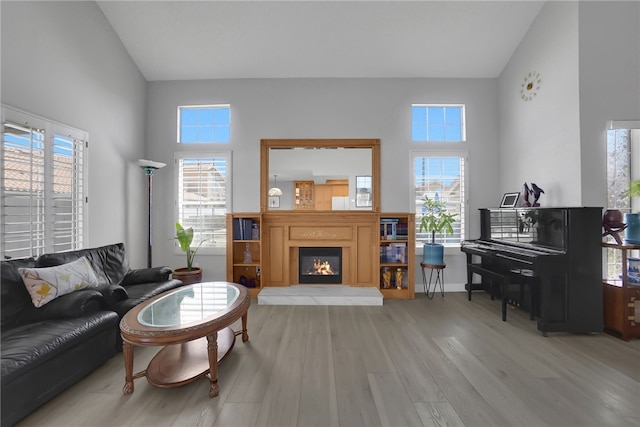 living area with high vaulted ceiling, light wood-style flooring, a healthy amount of sunlight, and a warm lit fireplace
