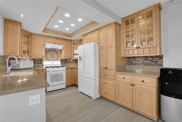 kitchen with a raised ceiling, a sink, white appliances, under cabinet range hood, and recessed lighting