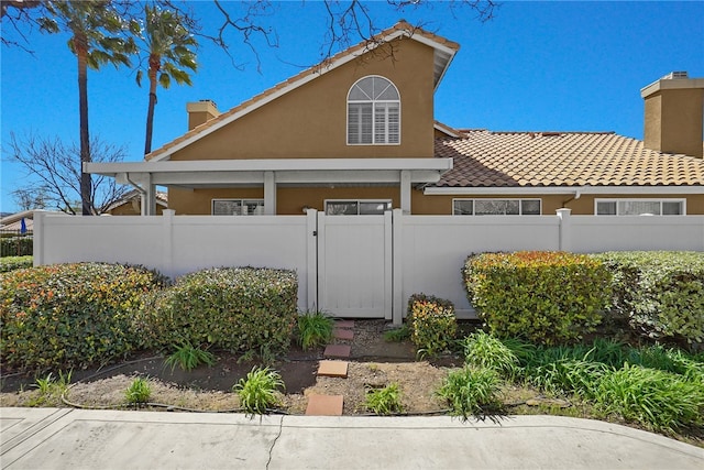 view of front of house featuring a chimney, a tile roof, a fenced front yard, stucco siding, and a gate