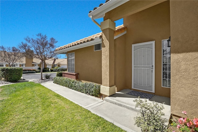 view of exterior entry featuring stucco siding and a lawn