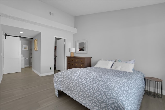 bedroom with baseboards, a barn door, visible vents, lofted ceiling, and wood finished floors