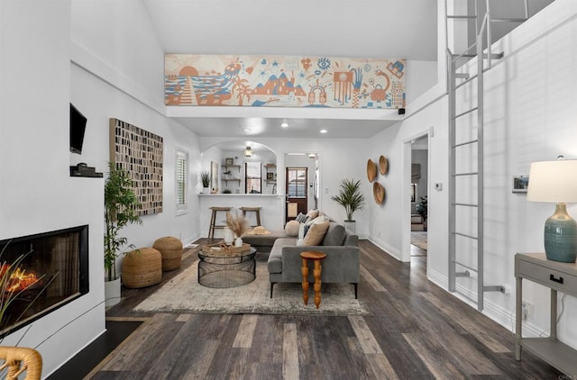 living room with a towering ceiling, baseboards, a lit fireplace, and wood finished floors