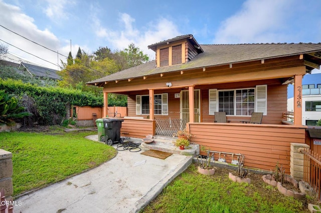 back of house with covered porch, fence, and a yard