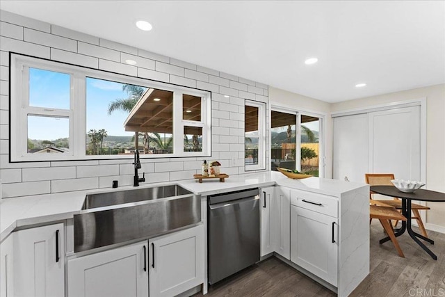 kitchen with dark wood-style floors, a sink, backsplash, a peninsula, and stainless steel dishwasher