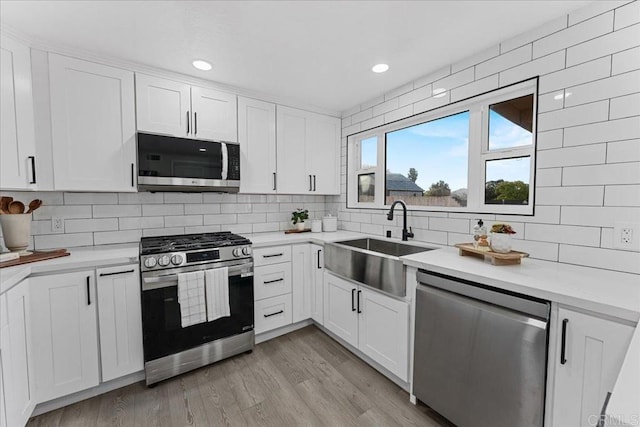 kitchen featuring white cabinetry, decorative backsplash, a sink, appliances with stainless steel finishes, and light countertops