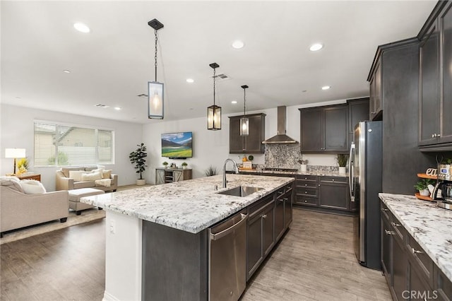 kitchen with a sink, wall chimney range hood, open floor plan, light wood finished floors, and stainless steel appliances
