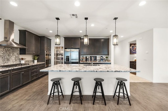 kitchen featuring wall chimney exhaust hood, a kitchen breakfast bar, visible vents, appliances with stainless steel finishes, and a sink