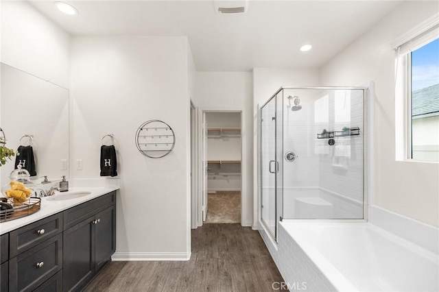 full bathroom featuring a garden tub, vanity, a spacious closet, wood finished floors, and a stall shower