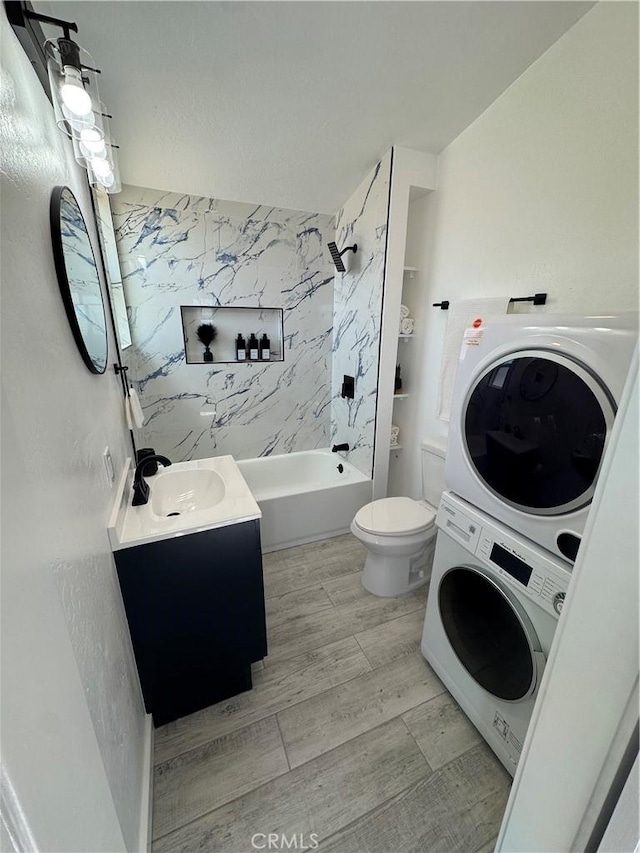 bathroom featuring wood finished floors, vanity, washtub / shower combination, stacked washer / drying machine, and toilet