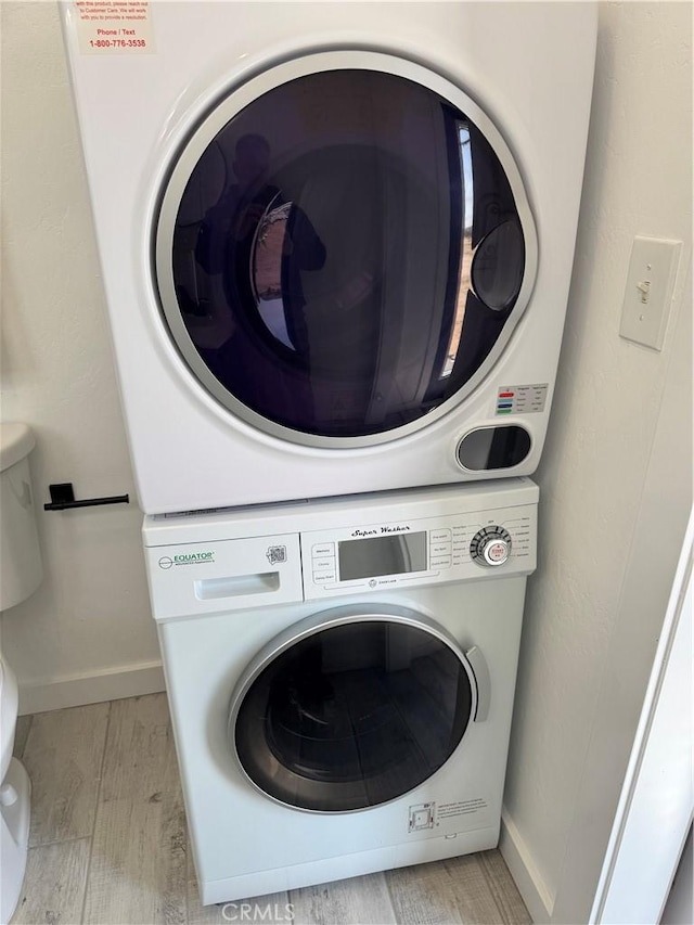 washroom featuring light wood-style flooring, baseboards, stacked washer / dryer, and laundry area