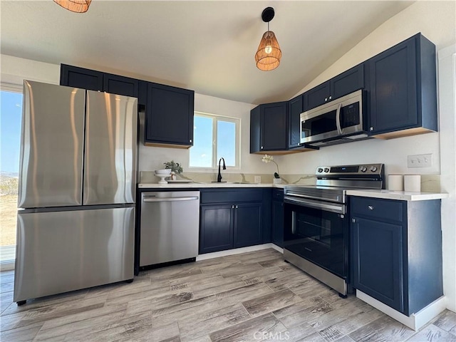kitchen featuring blue cabinets, stainless steel appliances, a sink, vaulted ceiling, and light countertops