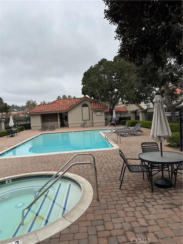 pool with fence, a community hot tub, and a patio area
