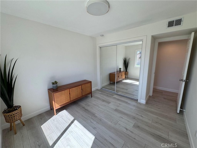 bedroom with a closet, visible vents, light wood finished floors, and baseboards