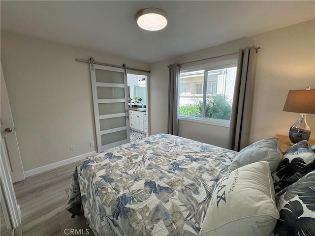 bedroom featuring a barn door, baseboards, and light wood finished floors