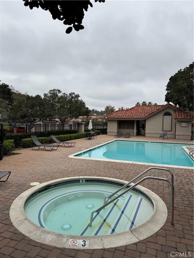 community pool with a hot tub, a patio, and fence