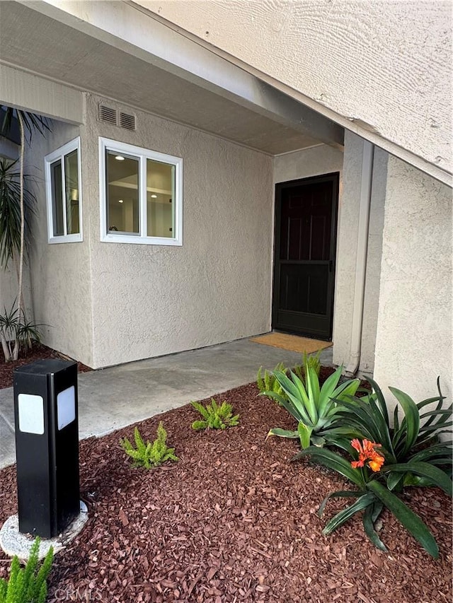 view of exterior entry featuring visible vents and stucco siding