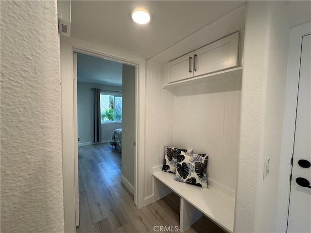 mudroom featuring wood-type flooring, baseboards, a textured wall, and visible vents