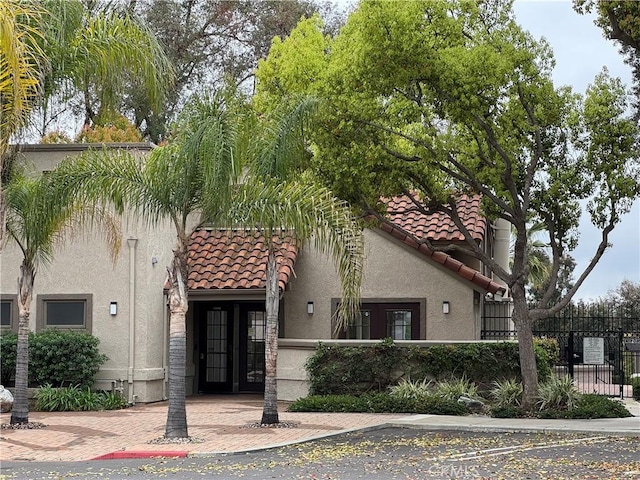 view of front of property with stucco siding, a tiled roof, and fence private yard