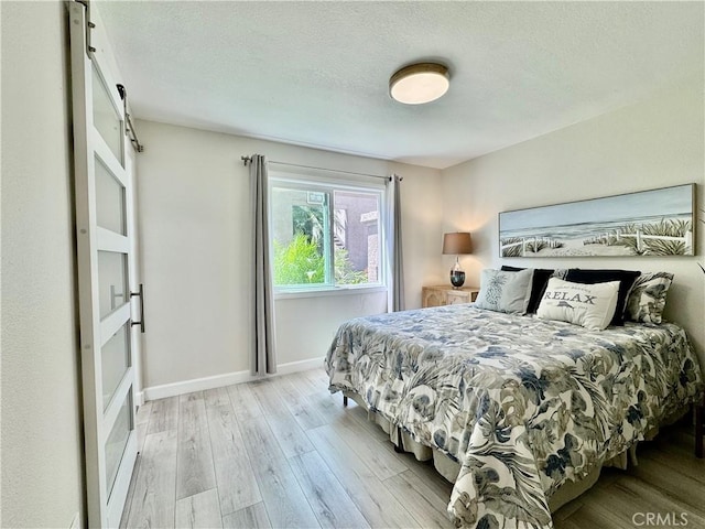 bedroom with a barn door, a textured ceiling, light wood finished floors, and baseboards