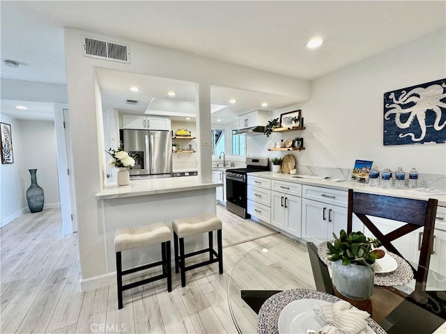 interior space featuring white cabinets, open shelves, visible vents, light wood-type flooring, and appliances with stainless steel finishes
