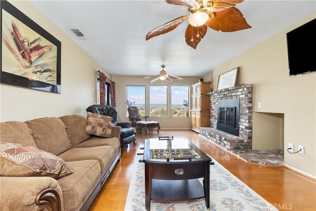 living area with visible vents, wood finished floors, a ceiling fan, and a brick fireplace