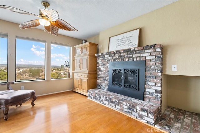 living room with a textured ceiling, light wood-style floors, a fireplace, and ceiling fan