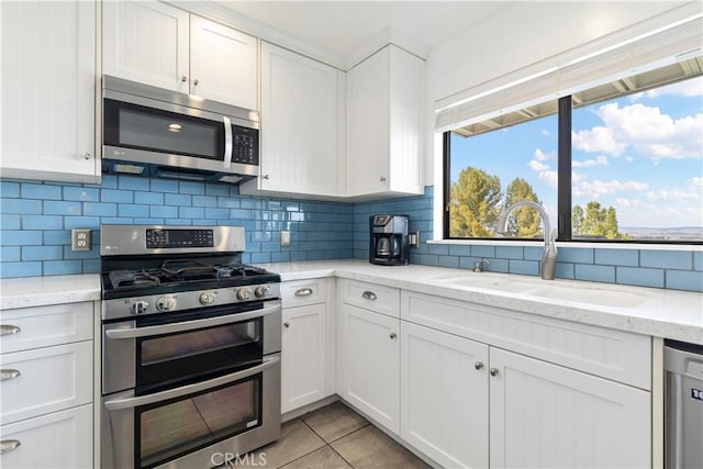 kitchen featuring backsplash, white cabinets, a sink, and stainless steel appliances