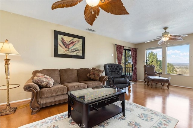 living area with baseboards, a textured ceiling, ceiling fan, and wood finished floors