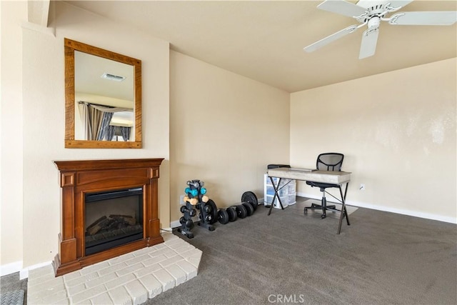 office with carpet flooring, visible vents, baseboards, ceiling fan, and a glass covered fireplace