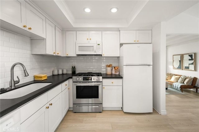 kitchen featuring a sink, dark countertops, a tray ceiling, and white appliances