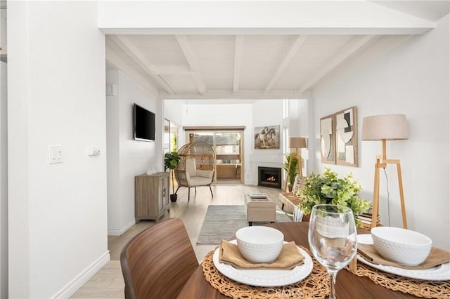 dining area with a warm lit fireplace, baseboards, beamed ceiling, and light wood finished floors