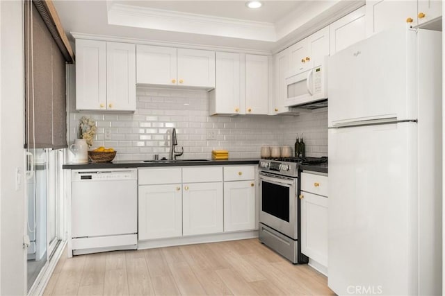 kitchen featuring white appliances, dark countertops, ornamental molding, and a sink