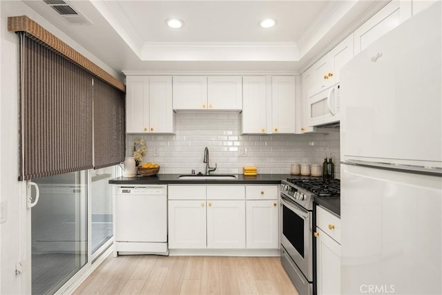 kitchen featuring white cabinetry, a tray ceiling, white appliances, a sink, and dark countertops