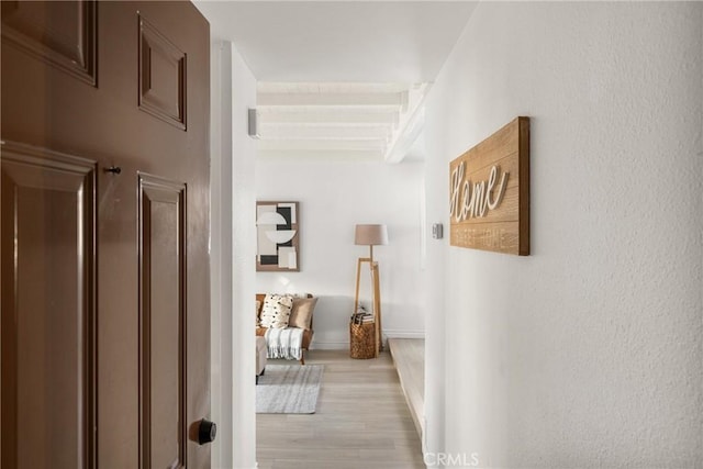 corridor with baseboards, light wood-style flooring, and beam ceiling