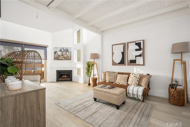 living area with attic access, light wood finished floors, a lit fireplace, and beam ceiling