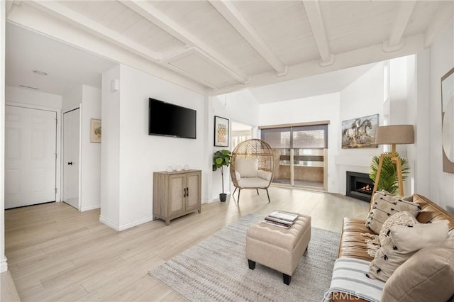living area with a lit fireplace, beam ceiling, light wood-style floors, and baseboards