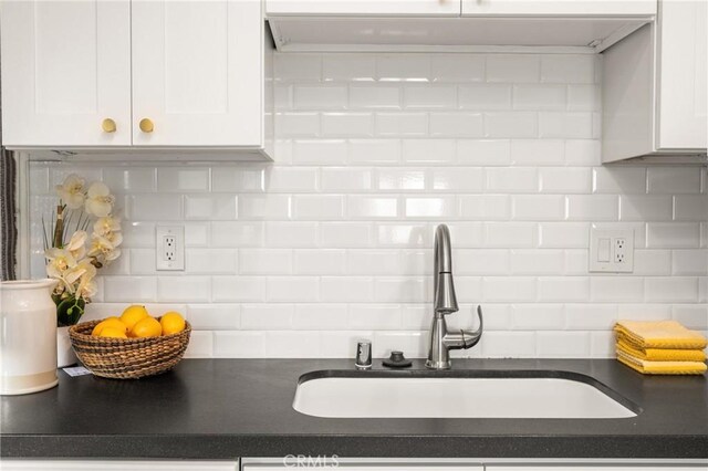 kitchen with white cabinets, a sink, dark countertops, and backsplash