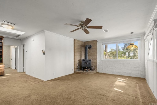 unfurnished living room with a ceiling fan, carpet floors, crown molding, and a wood stove