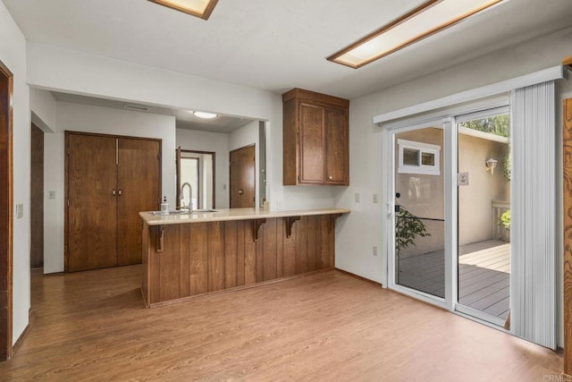kitchen with light countertops, light wood-style flooring, a kitchen bar, and a peninsula