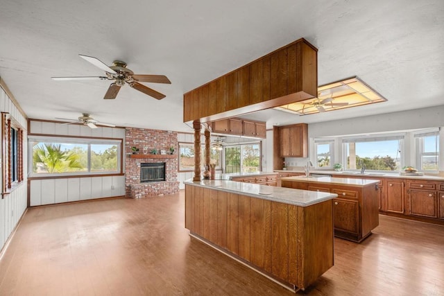 kitchen with an island with sink, brown cabinetry, a brick fireplace, and wood finished floors