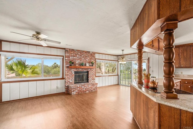 unfurnished living room featuring light wood finished floors, a wealth of natural light, a fireplace, and ceiling fan