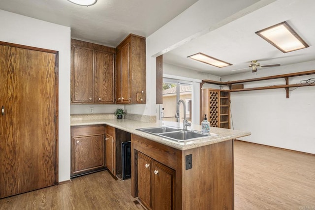 kitchen featuring light countertops, a sink, a ceiling fan, wood finished floors, and a peninsula