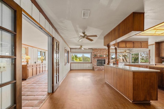 kitchen with visible vents, a fireplace, ceiling fan, wood finished floors, and brown cabinetry