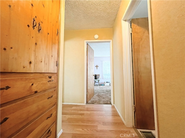 corridor featuring light wood finished floors, visible vents, a textured ceiling, and baseboards