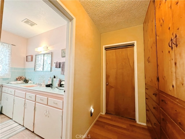 corridor with a textured ceiling, light wood finished floors, a sink, and visible vents