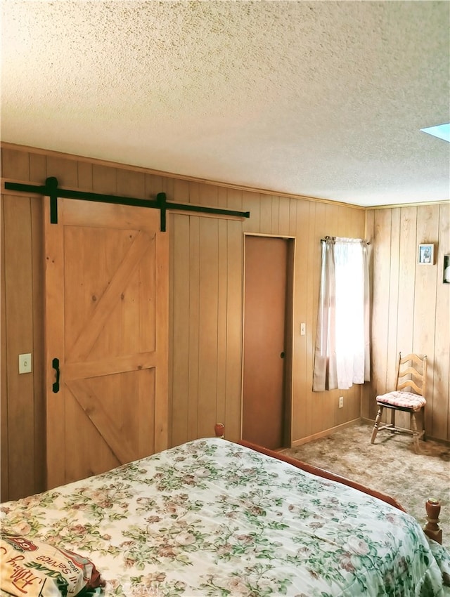 bedroom featuring a textured ceiling, wood walls, carpet flooring, and a barn door