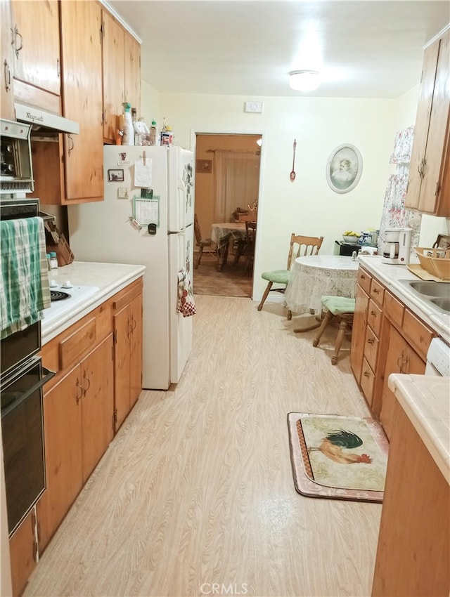 kitchen with a sink, light countertops, light wood-type flooring, white appliances, and under cabinet range hood